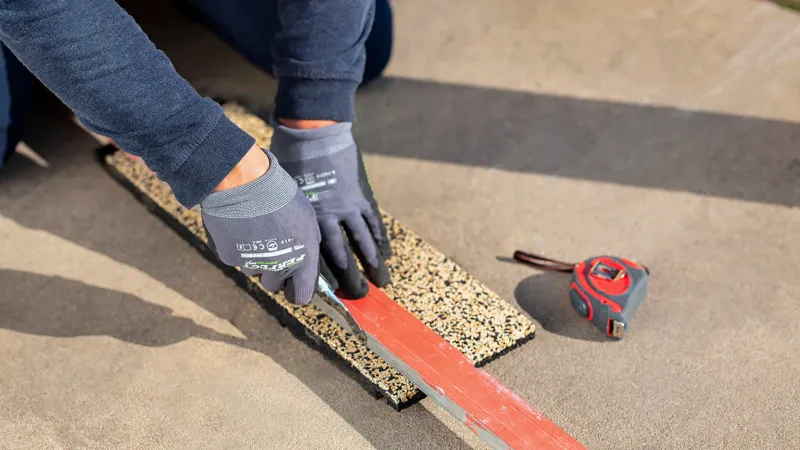 Mit entschiedenen, schnellen Bewegungen, bei denen das Messer an einer Schiene entlang geführt und bei jedem Schnitt immer etwas weiter in die Platte eindringt, kann man bei Gummigranulat-Platten ganz einfach gerade und saubere Schnitte ausführen.