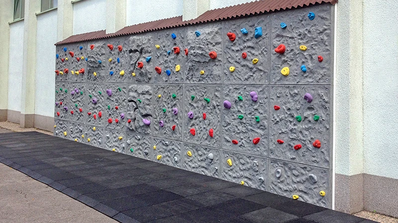 Een 6 meter lange en 3 meter hoge boulderwand, samengesteld uit losse segmenten, staat voor een lage wand. De hele ruimte voor en naast de boulderwand is bedekt met 100 mm dikke zwarte valbeschermingsplaten van WARCO. Anti-trip wiggen van rubbergranulaat zorgen voor een struikelvrije overgang van de in elkaar grijpende bestrating naar de valbeschermingsvloer.