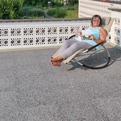 Op de foto is een ruim balkon te zien, dat is voorzien van grijze WARCO-vloerplaten. Iemand zit comfortabel in een schommelstoel, geniet van de zon en leest een boek. Het antislip en elastische oppervlak biedt zowel comfort als geluidsdemping. Bovendien is de vloer weerbestendig, robuust en onderhoudsvriendelijk, wat hem ideaal maakt voor langdurig gebruik. Zo ontstaat een uitnodigende buitenruimte om heerlijk te ontspannen.