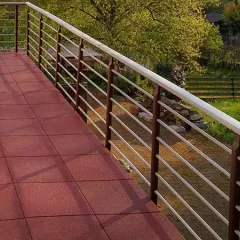 Op de foto zie je een ruim balkon met rode WARCO-vloerplaten. Het moderne hekwerk biedt vrij zicht op de tuin en zorgt voor een open sfeer. Dankzij de antislip- en weerbestendige eigenschappen en de elastische structuur biedt deze vloer veiligheid en comfort. Bovendien is hij eenvoudig te onderhouden en duurzaam, waardoor de buitenruimte uitnodigt tot ontspanning en lang plezier garandeert.