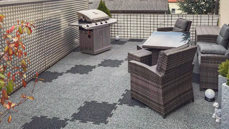 Op deze foto zie je een ruim dakterras met grijze WARCO-puzzeltegels. De antislipstructuur zorgt voor een veilige en comfortabele ondergrond. Weerbestendige rotanmeubels en een barbecue completeren de inrichting en nodigen uit tot gezellige bijeenkomsten. De slijtvaste vloer is eenvoudig te plaatsen en ideaal voor buitenruimtes dankzij het onderhoudsvriendelijke en weersbestendige materiaal. Zo ontstaat een uitnodigende plek om te ontspannen en te genieten.