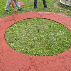 Een rode cirkel van WARCO-platen wordt op een stuk gazon gelegd, in het midden waarvan een speeltoestel wordt geïnstalleerd.