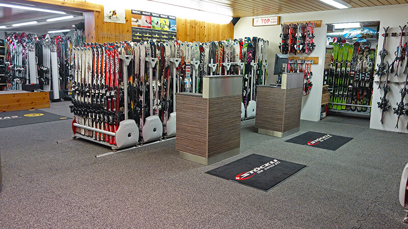 Derrière deux comptoirs du magasin de ski Gaby Sports se trouvent des stands présentant différents modèles de ski. Le sol est recouvert de dalles intérieures d’exposition à clipser de WARCO en couleur Marocco.