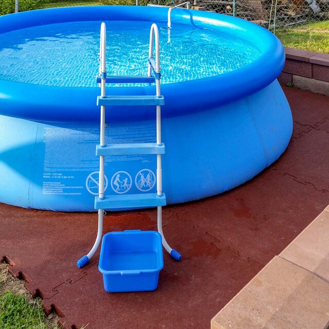 Dans un coin du jardin, la piscine gonflable est posée sur le sous-plancher pour piscine WARCO en couleur rouge brique.