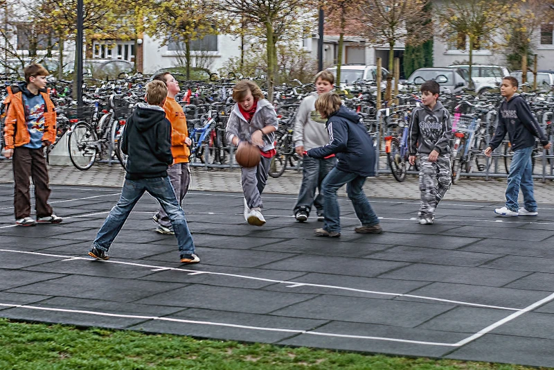 Een groep jongeren speelt met veel enthousiasme basketbal op een buiten basketbalveld gemaakt van groene ballenborden van WARCO.