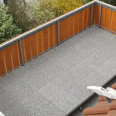 Op de foto is een ruim balkon te zien, dat is voorzien van grijze WARCO-vloerplaten. De omlopende houten bekleding zorgt voor privacy en sluit mooi aan bij de moderne vloer. Dankzij de antislip- en weerbestendige eigenschappen is deze vloer ideaal voor buitengebruik. Bovendien is hij elastisch en vangt hij stappen aangenaam op. Zo ontstaat er een comfortabele en onderhoudsvriendelijke buitenruimte waar men heerlijk kan ontspannen.