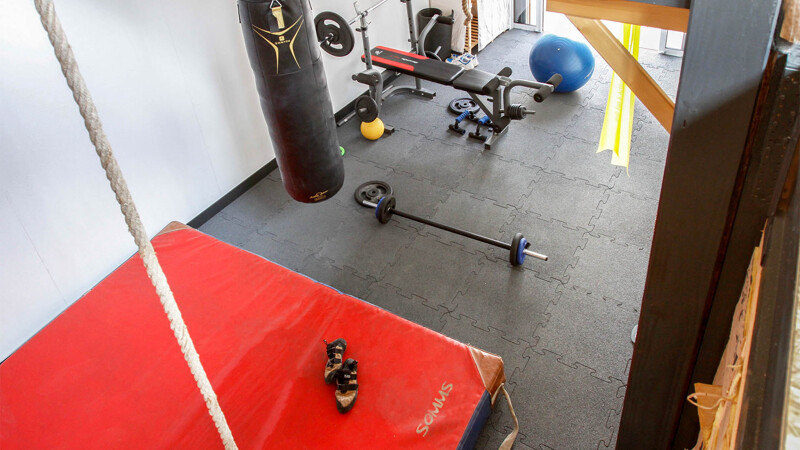 Zicht van bovenaf in en op een home gym, d.w.z. een privé fitnessruimte in huis. Verschillende fitnessapparaten zijn geplaatst op de zwarte fitnessmatten van WARCO met een puzzelrand.