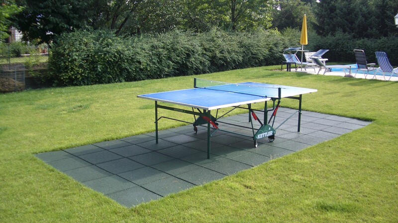 Unter einer Tischtennisplatte im Garten liegt ein Sportboden aus grünen WARCO Fallschutzplatten.