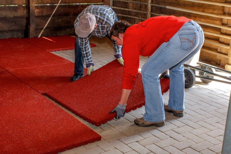 Deux hommes posent les tapis d'écurie de WARCO de grand format dans un box à chevaux dont le sol est déjà pavé de béton.