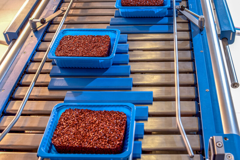 Des pièces moulées faites de granulés de caoutchouc de couleur rouge sont placées dans le plateau de vente sur la bande transporteuse de la machine emballage.
