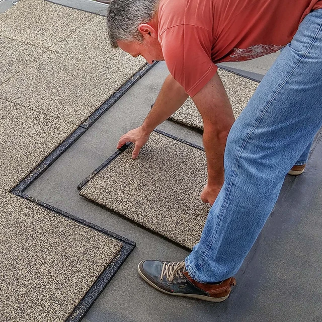 Un homme pose les dalles de terrasse WARCO directement sur une terrasse scellée et nivelée avec du feutre de toiture.