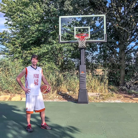Sur un terrain de basket dans le jardin avec des dalles de jeu de ballon WARCO en vert gazon, il y a un grand joueur de basket. Le bon rebond du ballon réponde aux exigences des joueurs de basket.