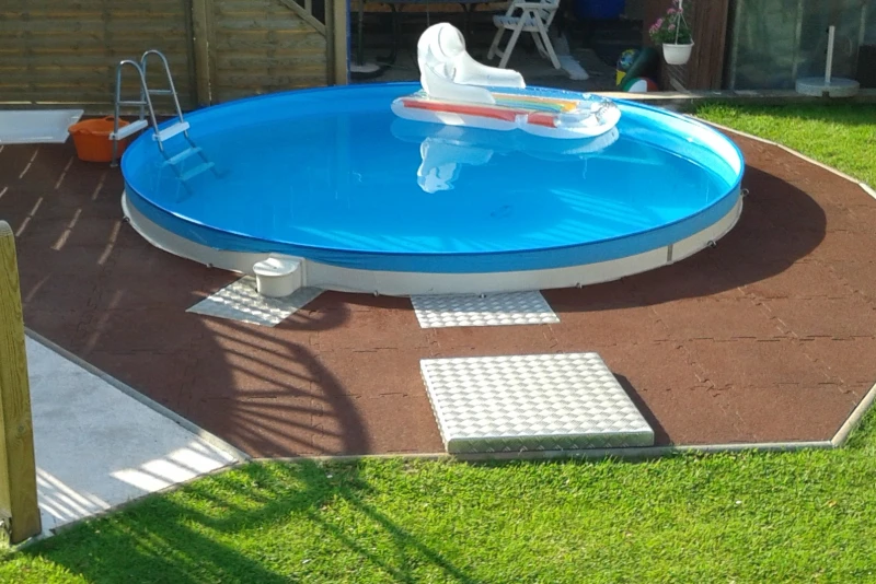 In het gazon in een hoek van de tuin werd een rond zwembad half in de grond verzonken. Rondom het zwembad werden rubbergranulaatplaten van WARCO gelegd.
