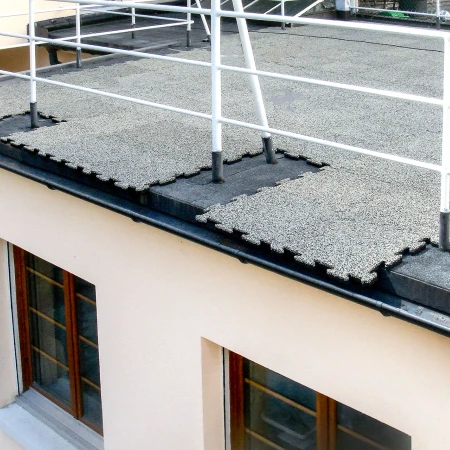 WARCO panelen in de kleur Grey Granite worden rechtstreeks op het dakvilt gelegd dat wordt gebruikt om het platte dak van een gebouw af te dichten. Omdat het gebied als terras wordt gebruikt, is er een reling op het platte dak. De randplaten worden op maat gesneden voor het gebied.