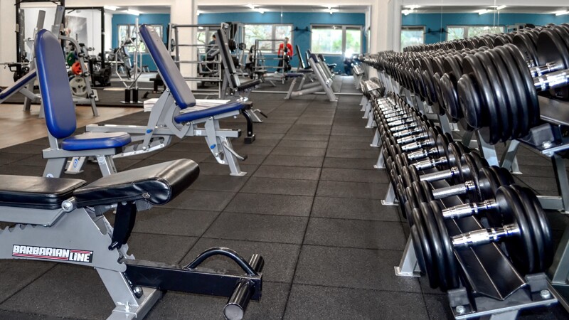 Dans une salle de musculation, plusieurs bancs inclinés pour entraînement des haltères sont placés sur un sol sportif WARCO.