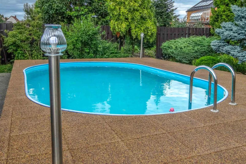 Een zwembad in de grond in de tuin heeft een omranding van terracotta zwembadtegels van WARCO. Achter het zwembad staan struiken en een hek.