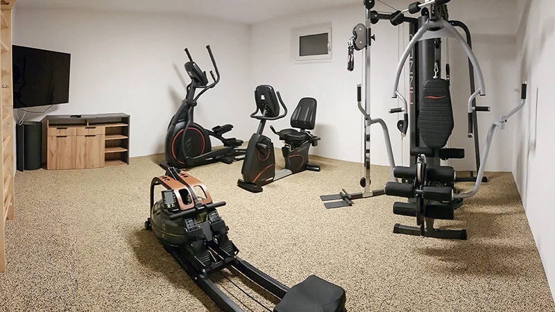 Sportschool aan huis met roeimachine, stepper en fitnessapparatuur op bruine Warco-vloer.
