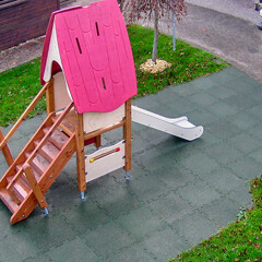 Roze huisje op groene Warco platen. Het speelhuisje heeft een trap en een glijbaan, staat op een grasveldje en staat in een tuin of kinderkamer.