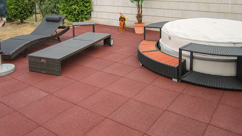Un vaste espace extérieur équipé de dalles de terrasse WARCO rouges en granulat de caoutchouc lié au PU, offrant une foulée confortable et une grande durabilité. L’aménagement comprend des meubles de jardin accueillants et un jacuzzi qui s’intègre harmonieusement à l’ensemble. La surface élastique amortit les pas, résiste aux intempéries et se nettoie facilement. Grâce à sa texture antidérapante, elle propose une solution attrayante pour se détendre avec style en plein air. Idéal pour les terrasses modernes alliant fonctionnalité et confort.