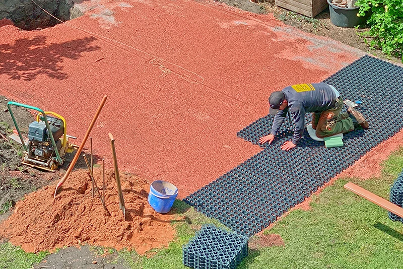 Un homme pose les dalles sportives WARCO en forme de puzzle en couleur vert gazon sur des grilles alvéolées en plastique remplies de gravier.