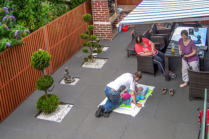 La famille profite sa terrasse conçue comme une oasis de bien-être. Le bébé est couché sur le revêtement de sol souple WARCO.