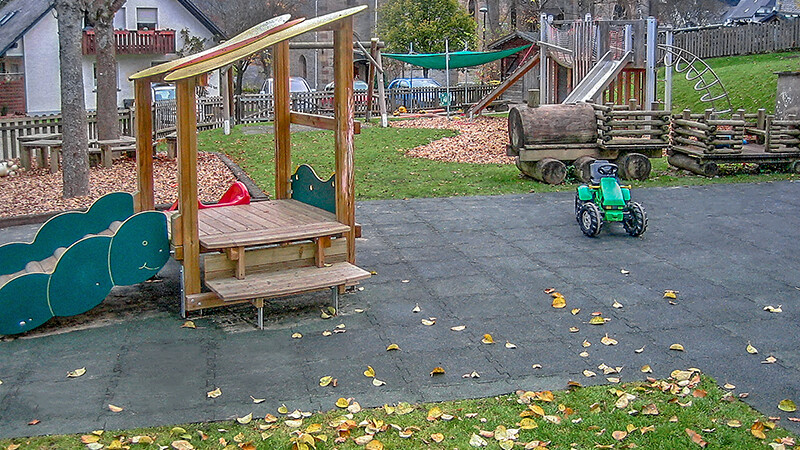 Speeltuin met houten spoorweg, glijbanen en steigers. Een groene speeltractor staat op zwarte WARCO latten.