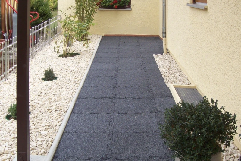Une trottoir faite de dalles en caoutchouc WARCO en Anthracite mène par le jardin moderne et élégant en gravier vers la porte entrée.